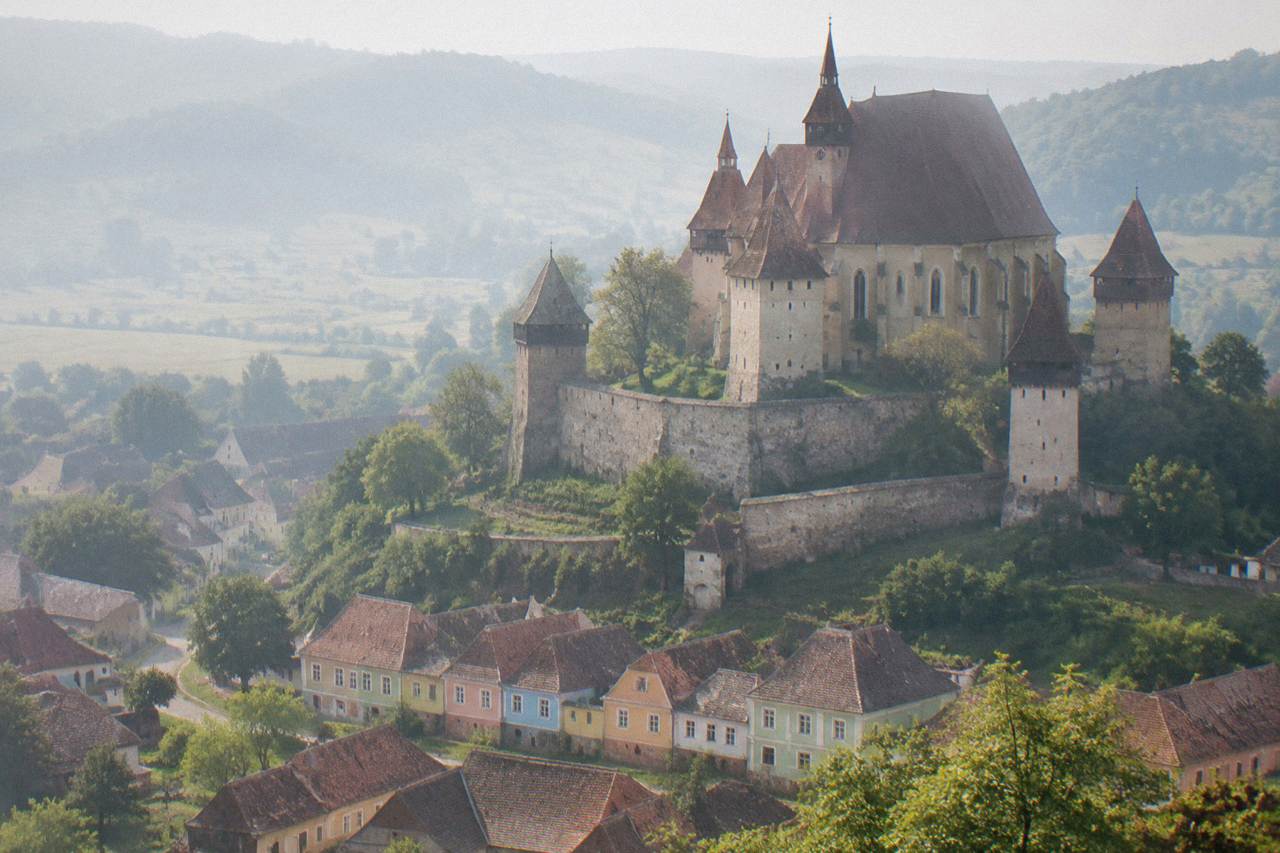 A fortified Saxon church with high defensive walls and towers rising above a Transylvanian village