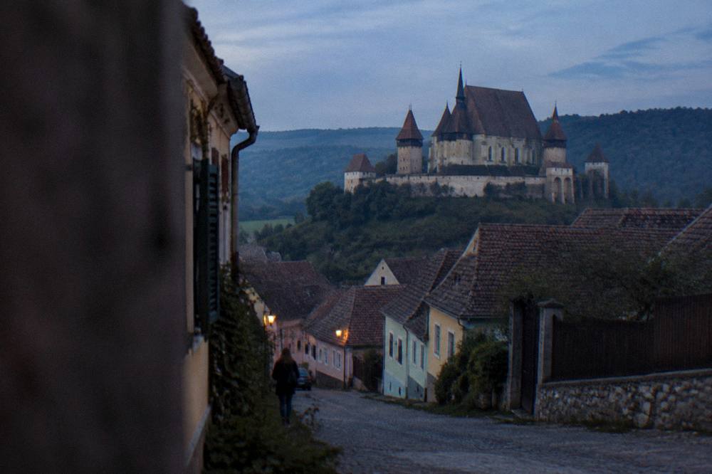 A quiet Transylvanian village street with traditional houses and hills behind