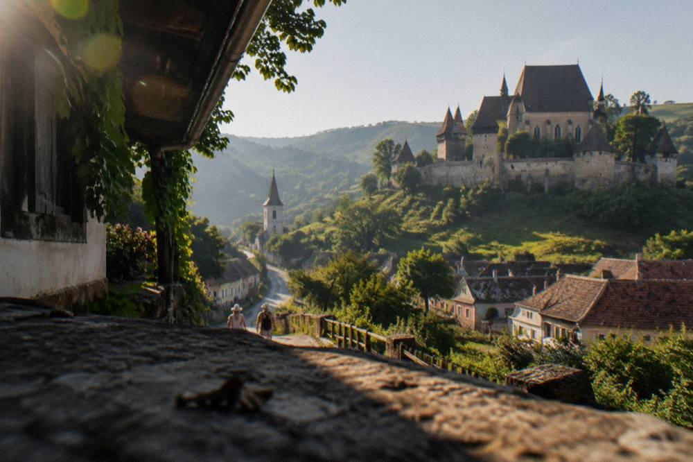 A country road winding between hills toward a village church tower in summer