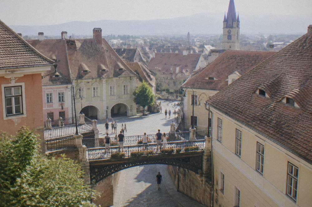 Visitors crossing a small iron footbridge between two old squares in Sibiu