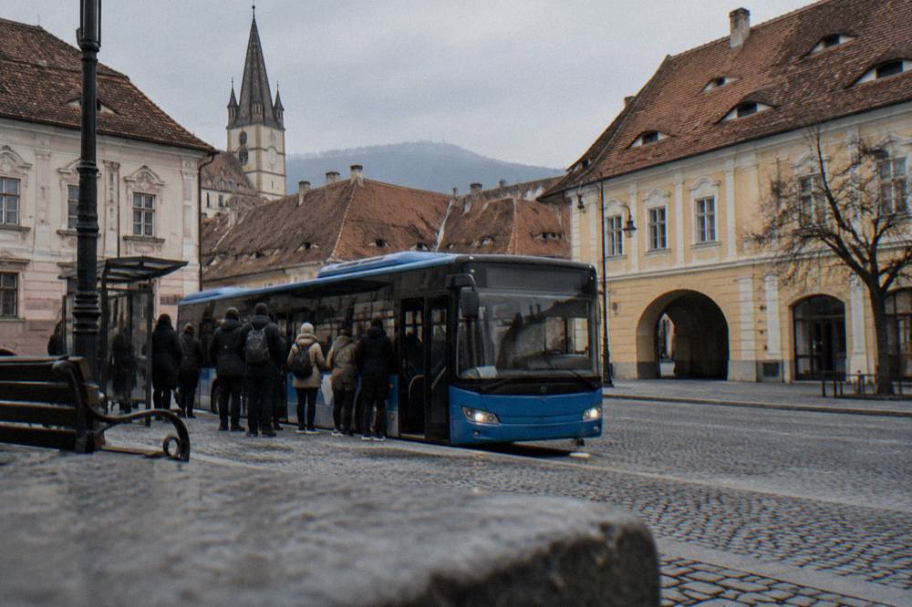 A blue city bus at a stop on a street in Sibiu with passengers waiting to board
