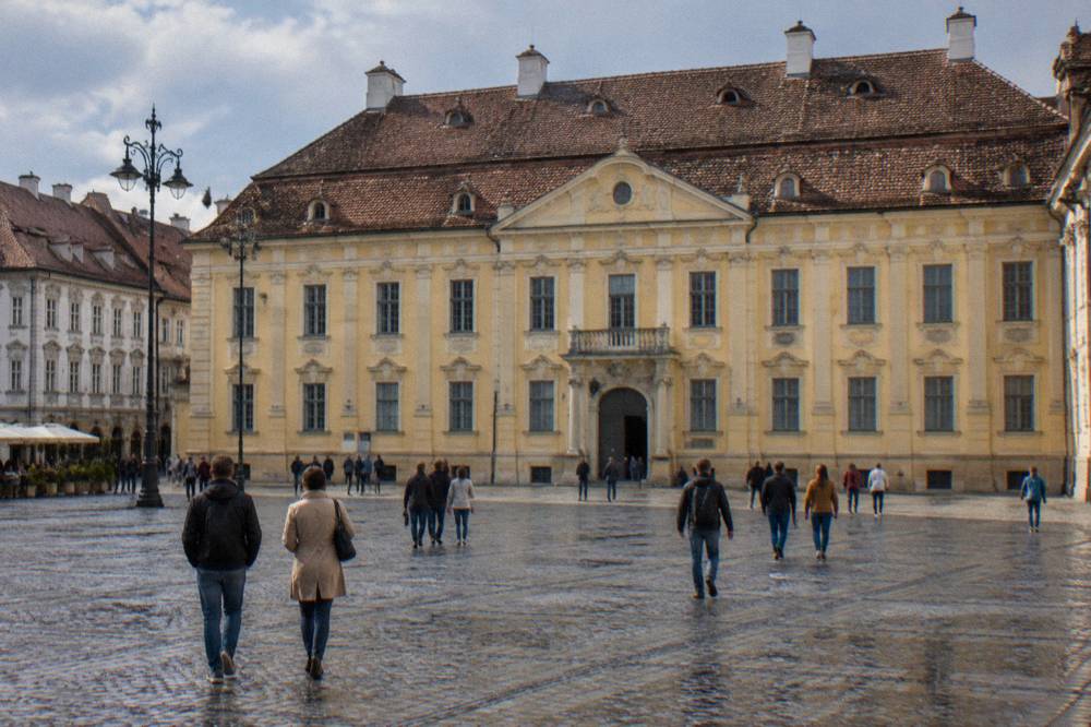 Visitors walking across Piața Mare in Sibiu with the Brukenthal Palace facade behind them
