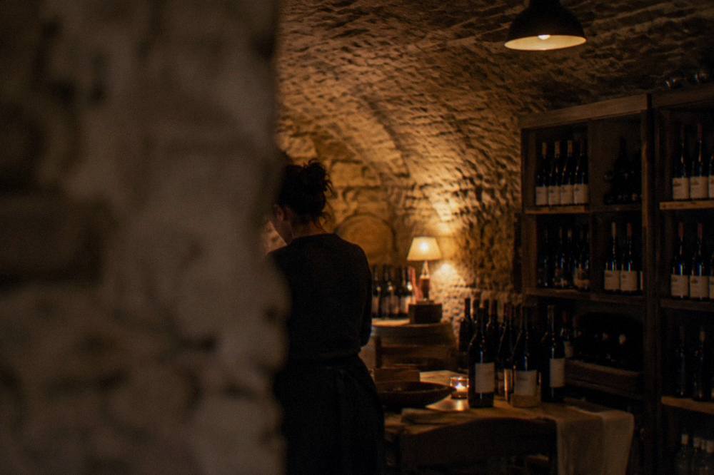 A row of wine bottles on shelves in a dim stone cellar