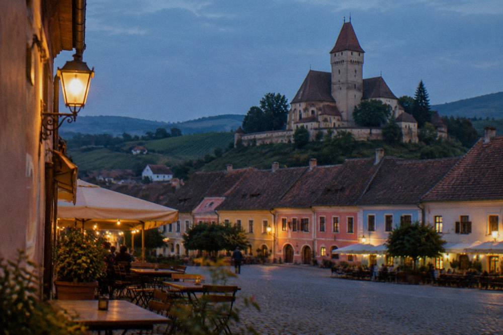 Evening lights over the coloured facades of a grand square with outdoor tables