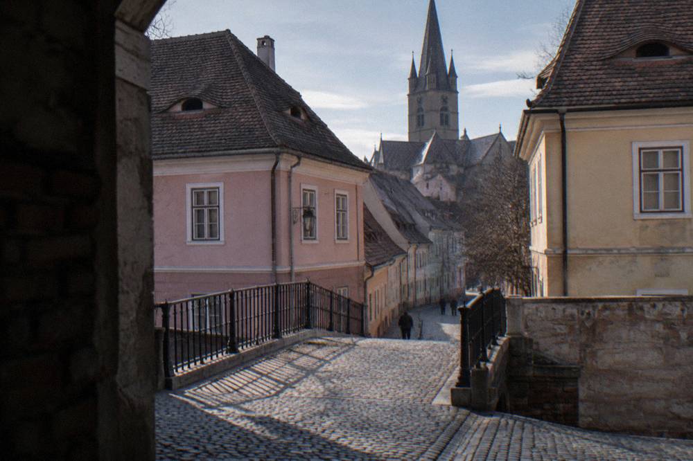 The iron Bridge of Lies spanning a narrow street between pastel houses in Sibiu