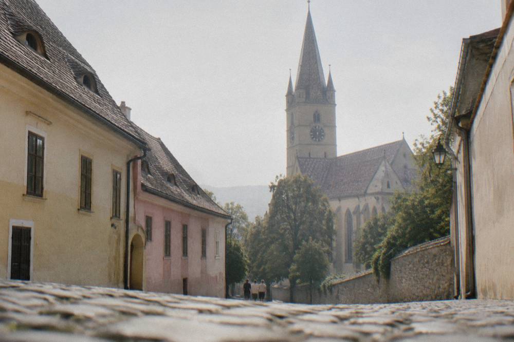A narrow village street with Saxon houses and a church tower behind trees in Transylvania