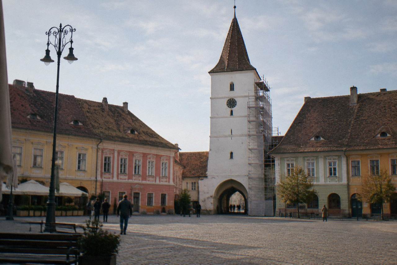 The wide open Grand Square of Sibiu with colourful baroque buildings and the Council Tower under restoration scaffolding