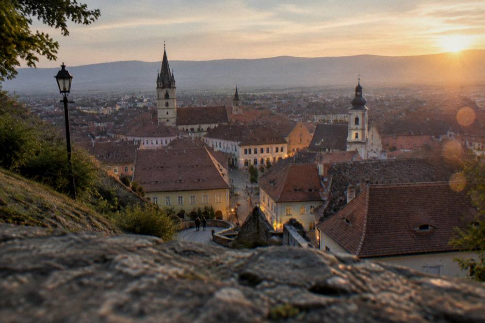 Evening lights over the rooftops and church towers of Sibiu seen from a hillside above the city