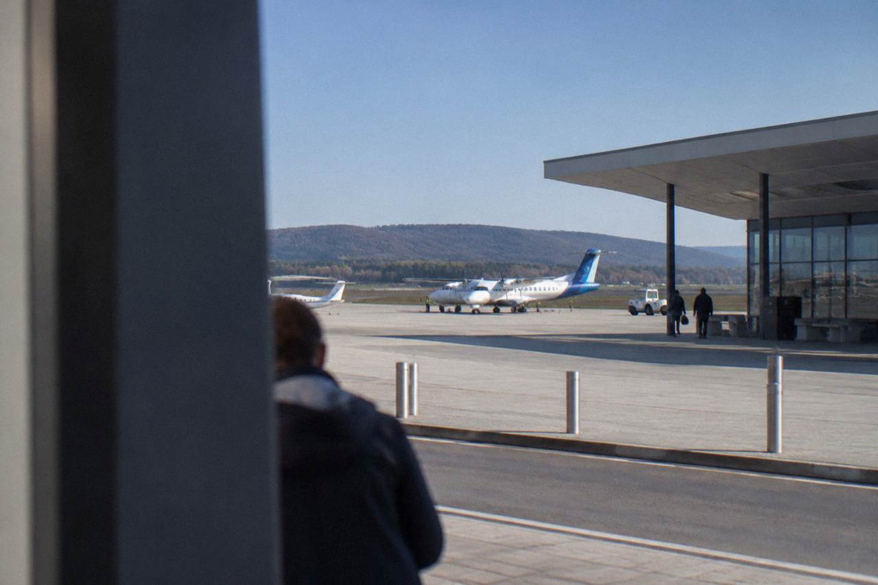 A small regional airport terminal building under a blue sky with parked aircraft on the apron