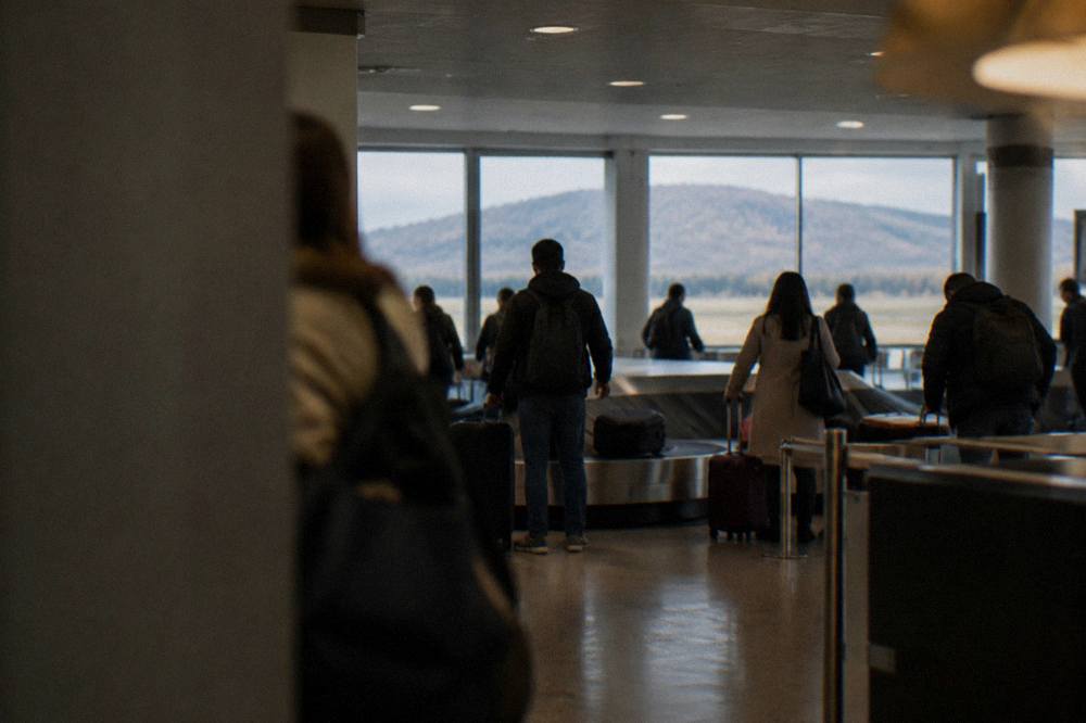 An airport arrivals hall with a small crowd collecting luggage around a carousel