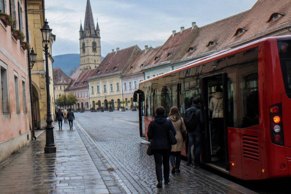 A red city bus parked at a stop on a street in Sibiu with passengers boarding