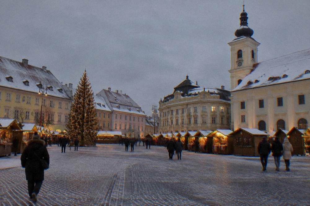 Wooden market stalls lit in the evening on a stone square.