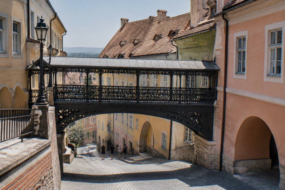 A covered iron footbridge linking two old town squares above a cobbled lane