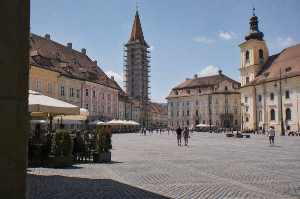 A tall medieval clock tower wrapped in scaffolding above a public square