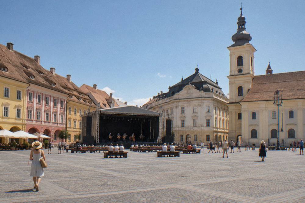 An outdoor theatre stage set up in a cobbled square surrounded by colourful baroque buildings