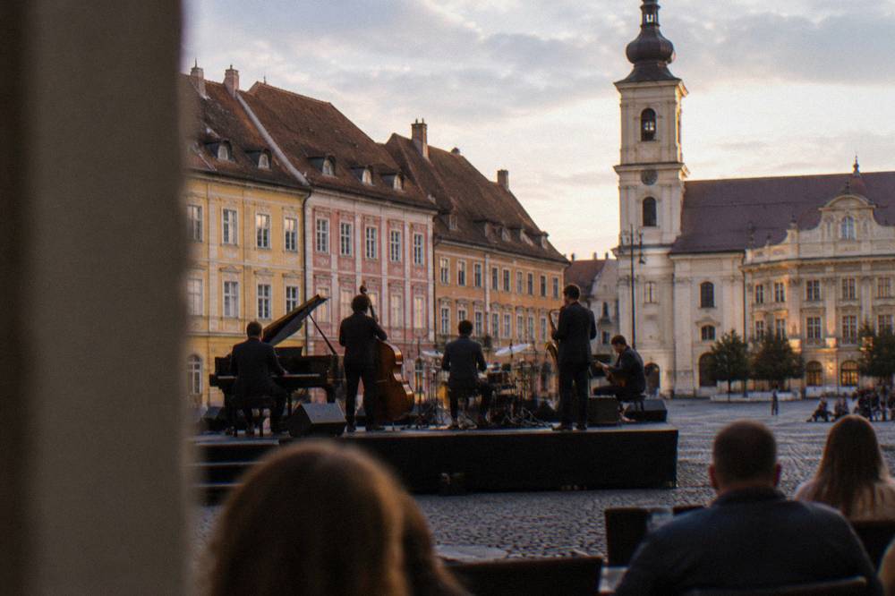 A jazz quintet performing on an outdoor stage at dusk in a Transylvanian city square