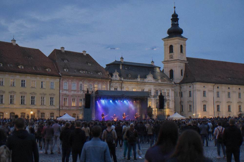 A large crowd watching a rock concert beneath the colourful facades of a historic square