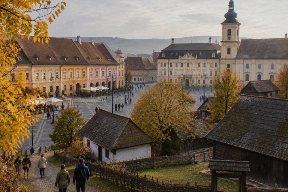 Visitors walking among wooden farmhouses and barns in an open-air ethnographic museum in autumn