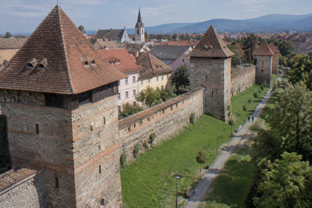 Medieval city wall towers of Sibiu with red-tiled roofs above a green lawn