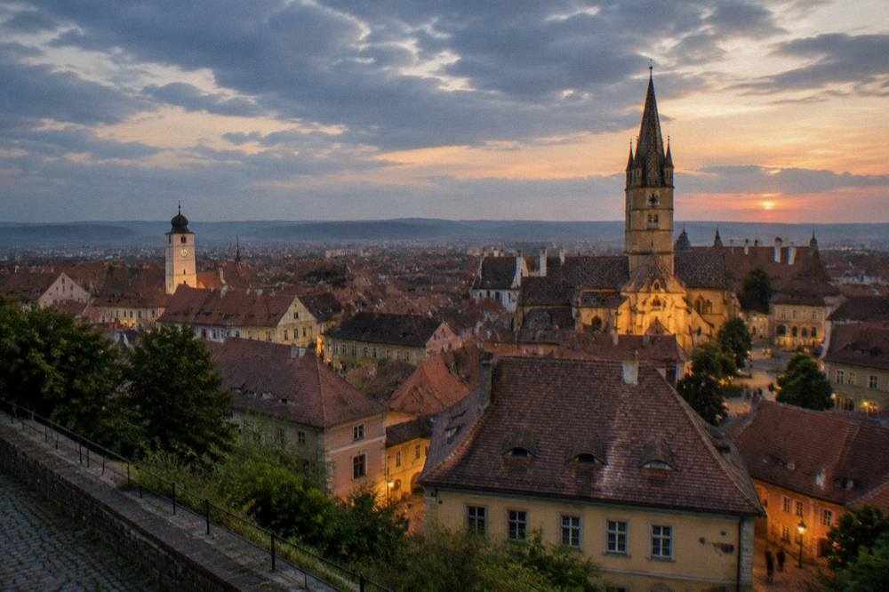 Evening panorama of Sibiu old town from a hill, with towers lit against a dusk sky