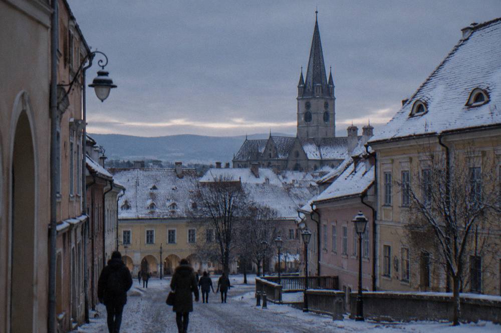 Snow-covered rooftops and the Lutheran church spire of Sibiu seen from a city street in winter light