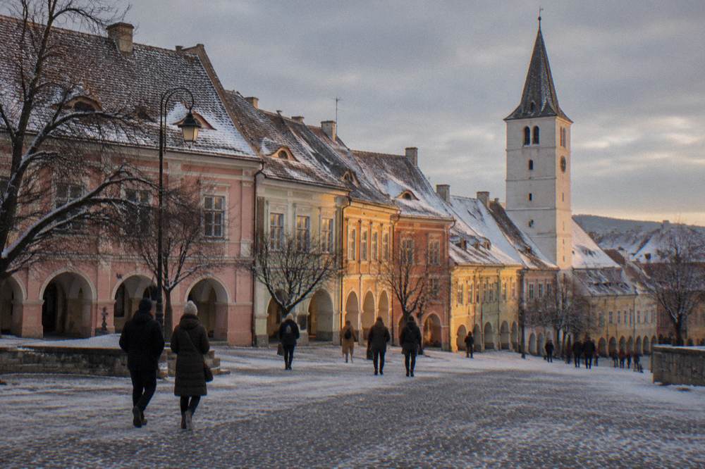 Visitors walking past the colourful baroque facades of Sibiu's Piața Mică under bare winter trees