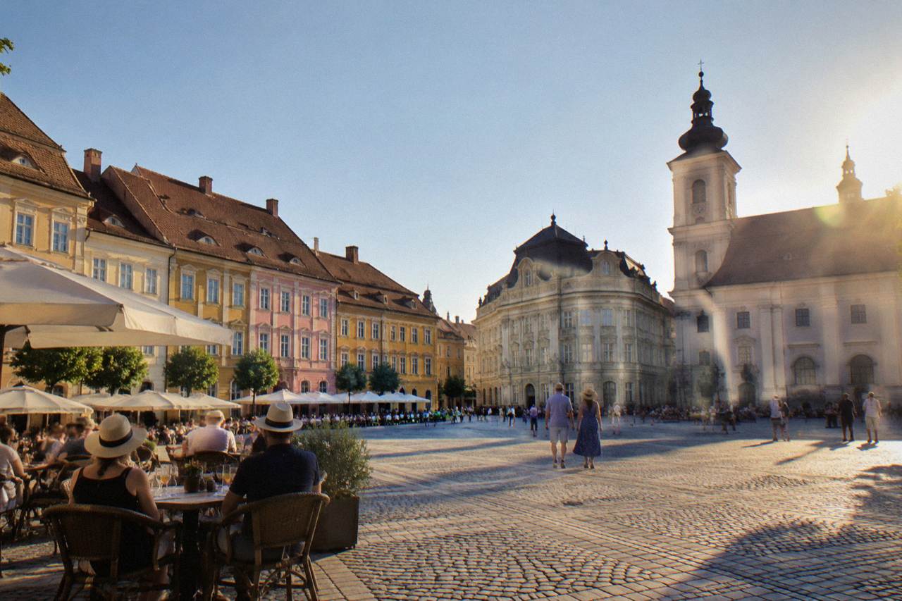 Sunlit Piața Mare in Sibiu with colourful facades and outdoor cafe tables
