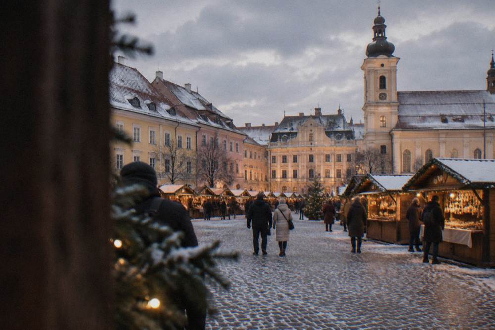Wooden Christmas market stalls with warm lights set out in a European town square at dusk in snow