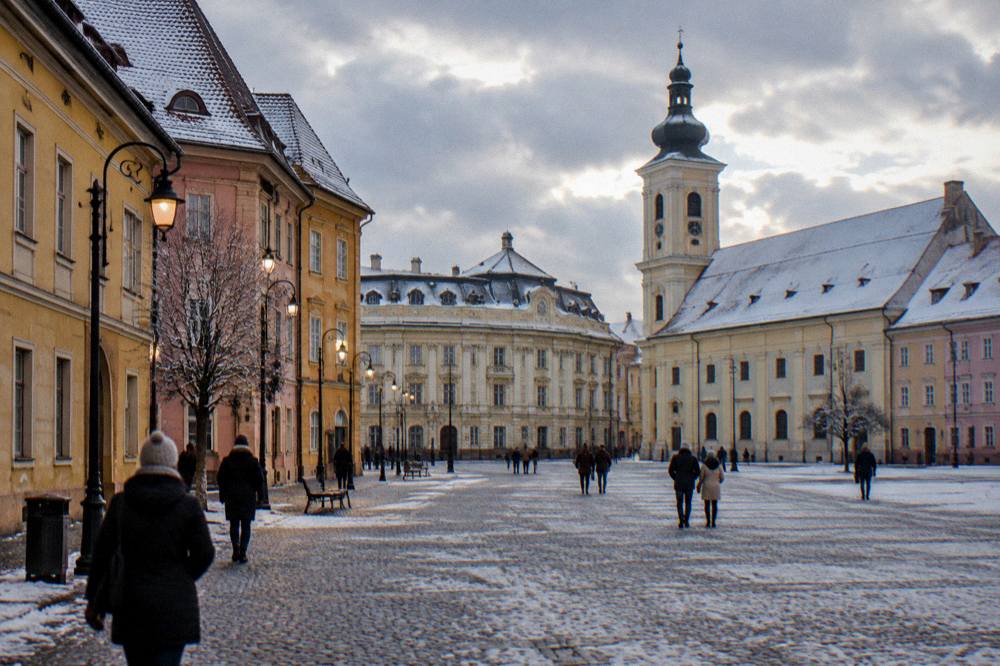 A pedestrian street of coloured old houses lit by lamps on a snowy evening in a Transylvanian town