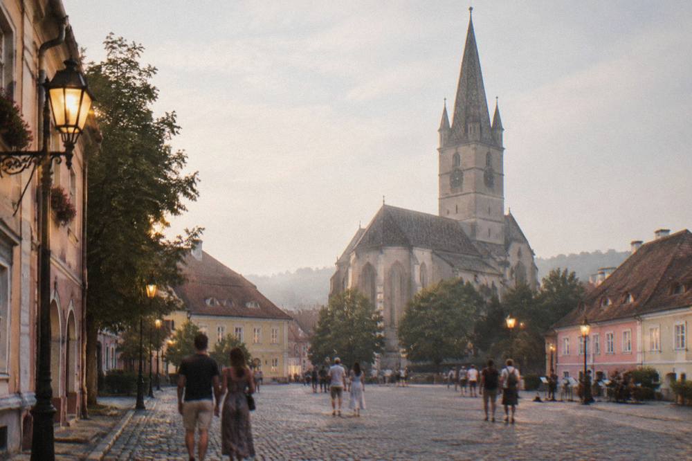 Visitors strolling through a lamplit medieval street in the evening with music stands in the distance