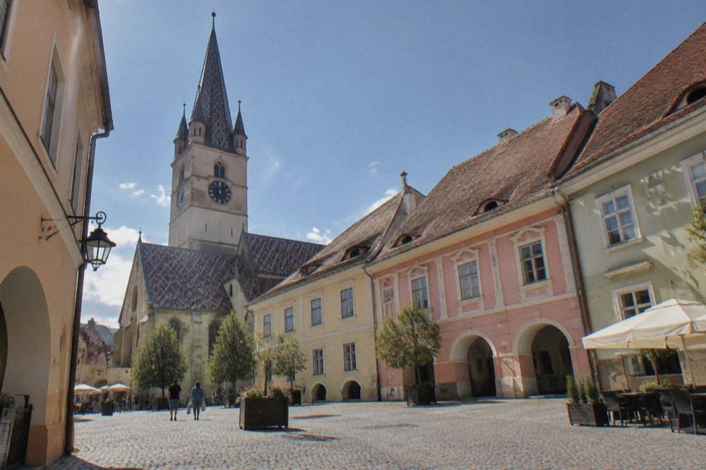 A cobblestone square in Sibiu with pastel merchant houses and a church tower