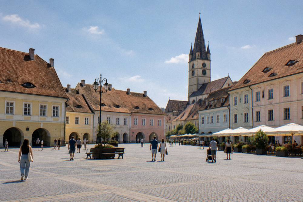 People strolling across a wide cobbled square ringed by historic buildings