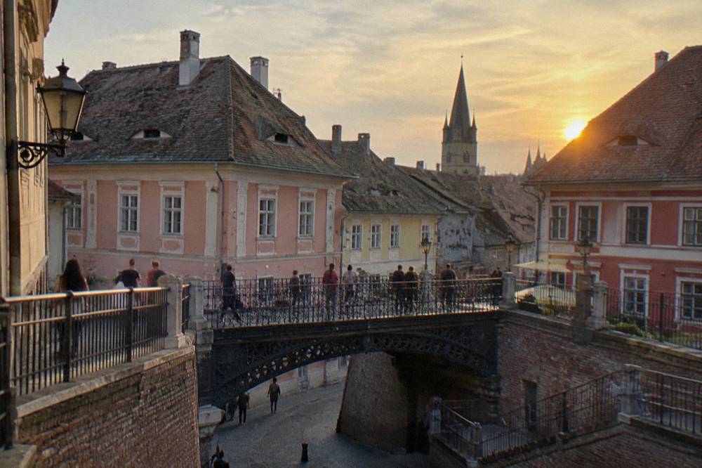 Iron footbridge and coloured facades above a narrow square in Sibiu at dusk