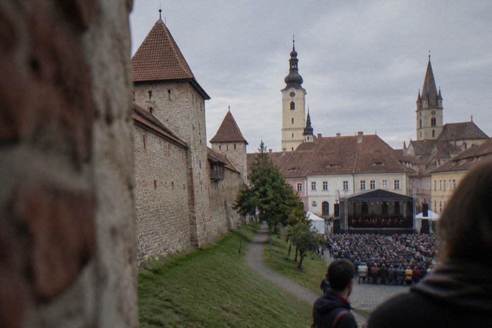 Open-air stage and audience in a historic square framed by church towers
