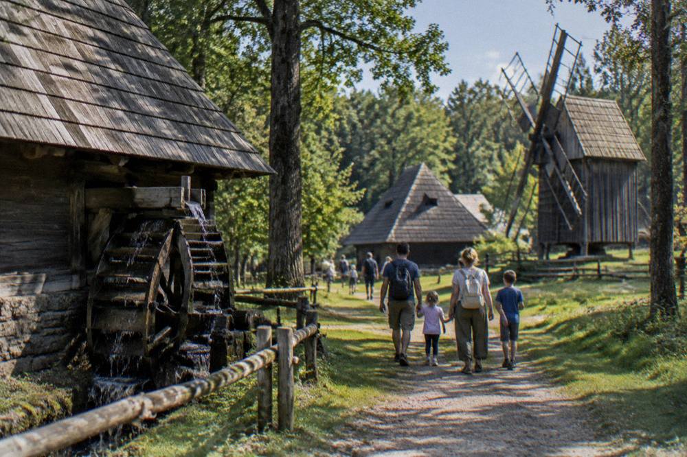 Families walking a forest path between traditional wooden houses at an open-air museum