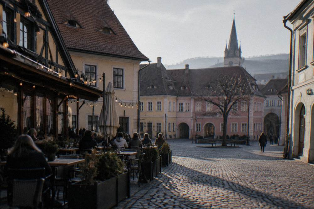 People seated at outdoor terrace tables under string lights beside old timber-framed buildings