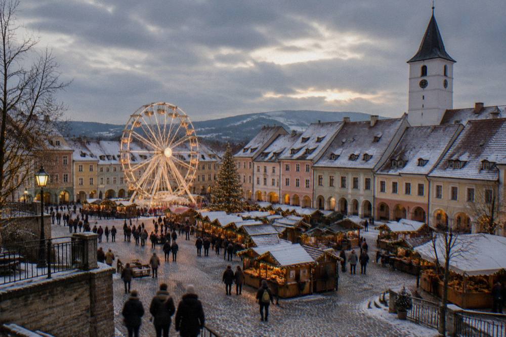 A Christmas market square at night with a lit ferris wheel and wooden stall roofs
