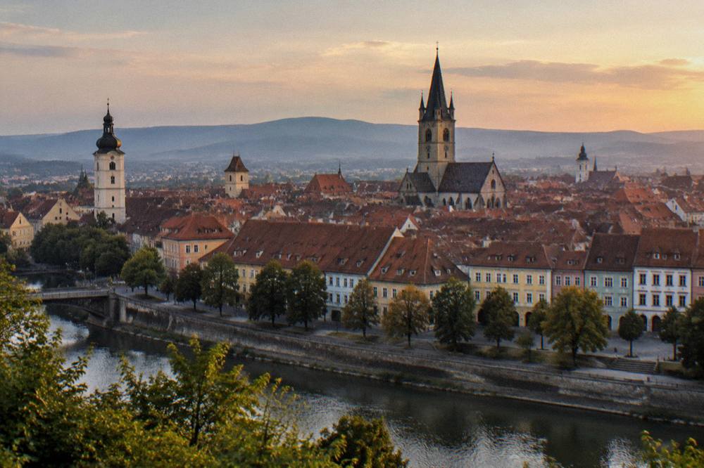 Evening panorama of Sibiu's old town towers and rooftops seen from a hillside across the river