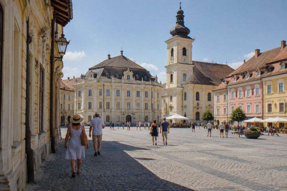 Visitors walking past a baroque art museum facade on one side of a grand square