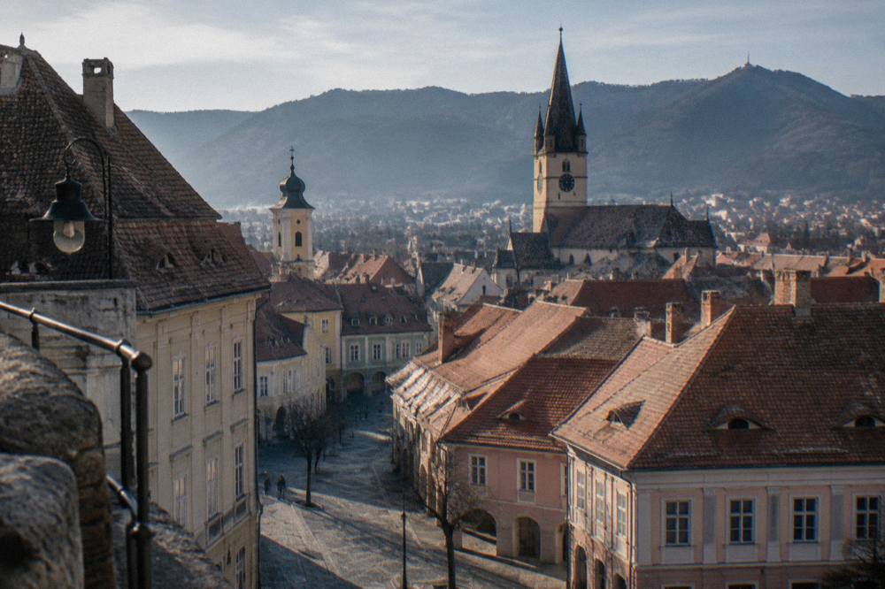 A panoramic view over a red-roofed old town toward dark forested mountains