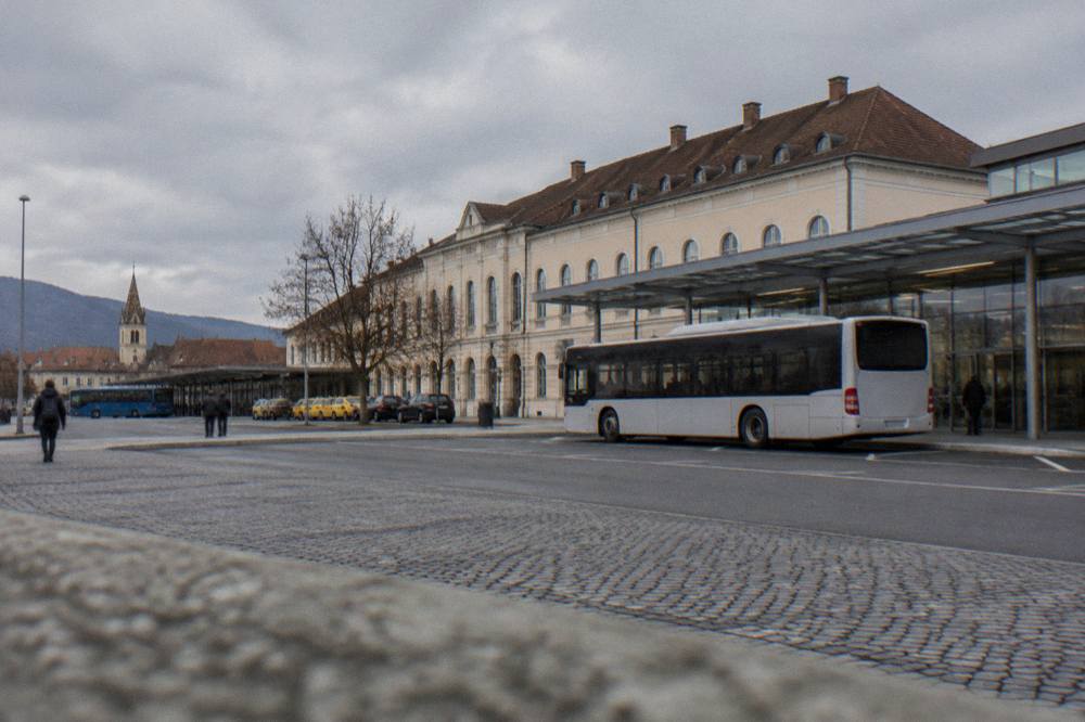 A city bus parked at a marked airport stop with glass terminal doors behind it
