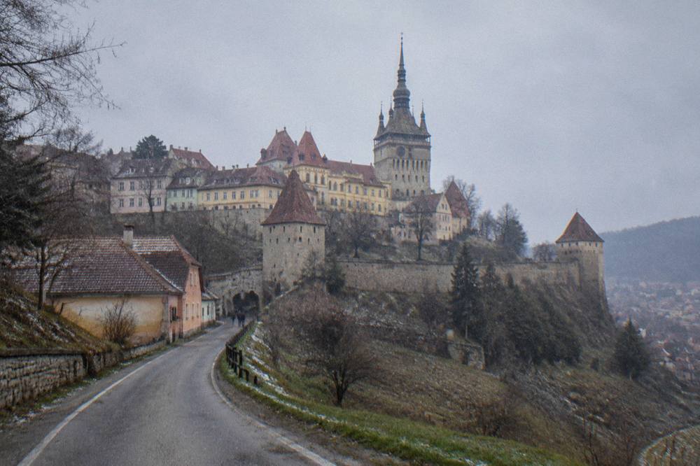 A country road winding through green hills toward a Transylvanian town