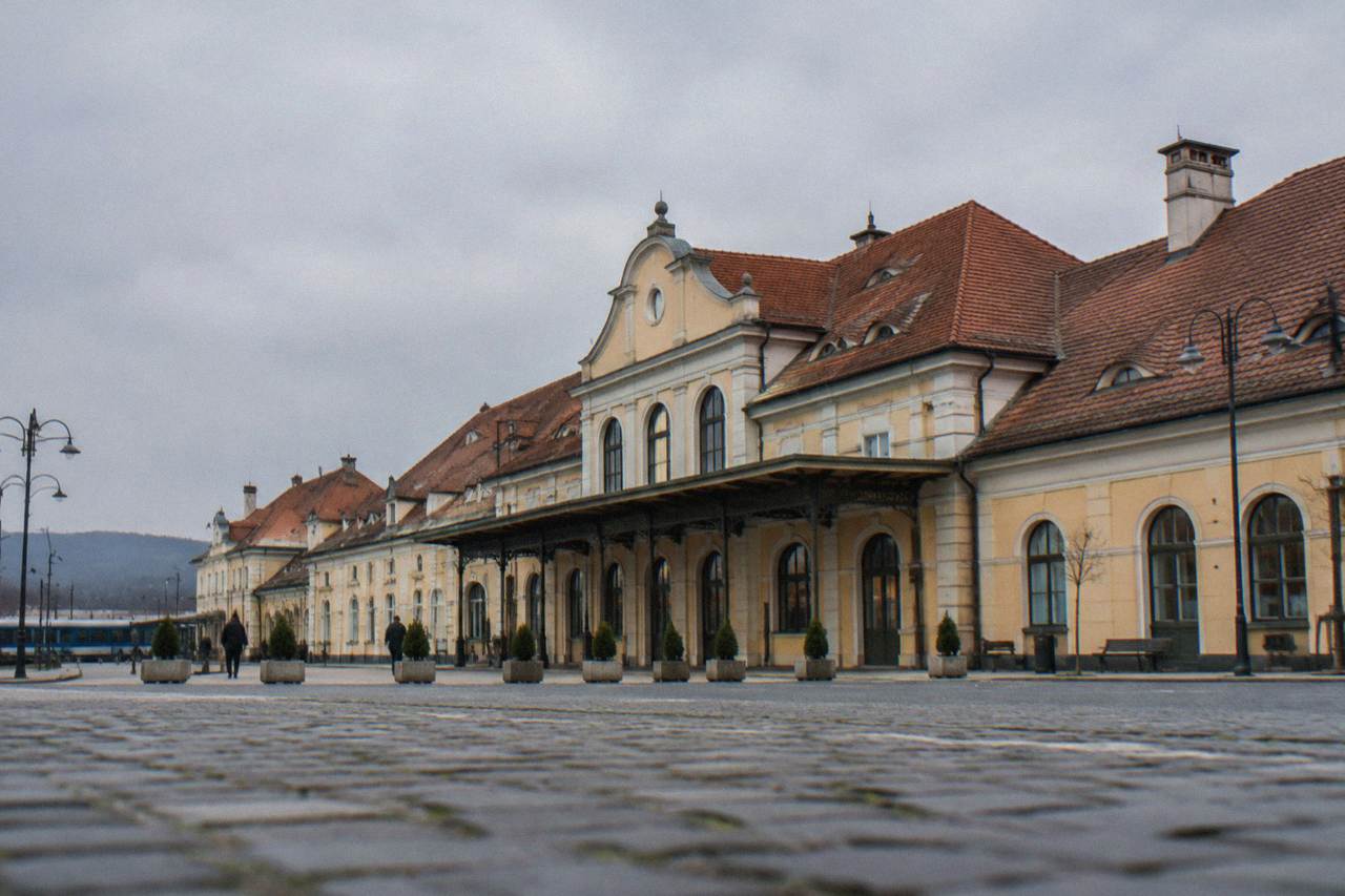 The front of Sibiu train station with its station name sign and people with luggage outside the entrance