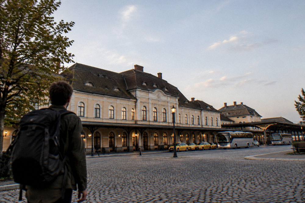 A traveller with a backpack looking at a departure board inside a Romanian railway station