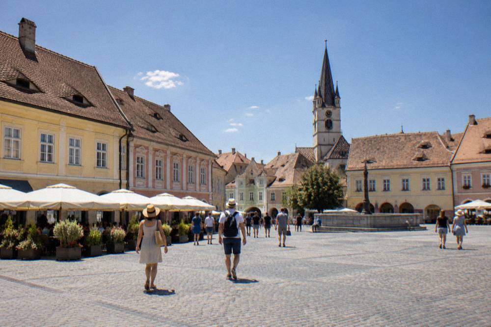 Visitors walking across a cobbled square in Sibiu under a clear blue summer sky