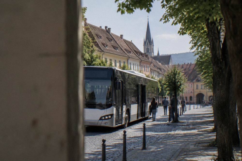 A city bus pulling up at a stop on a tree-lined street on the edge of Sibiu's old town