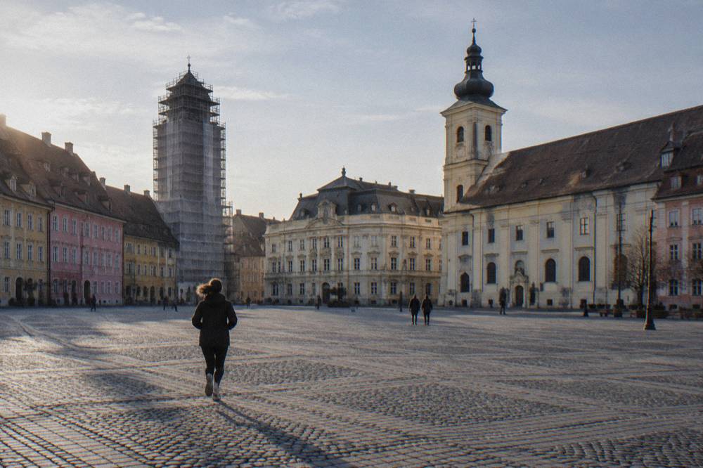 A tall medieval tower wrapped in scaffolding and protective netting beside a pastel square