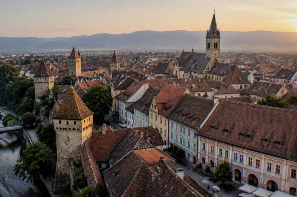 Aerial view of red rooftops and defence towers of a walled Transylvanian old town at dusk