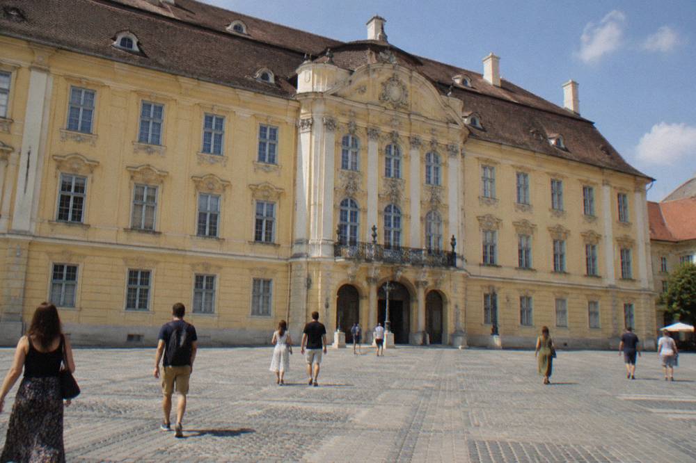 Visitors walking past the baroque facade of the Brukenthal Palace on the grand square in Sibiu