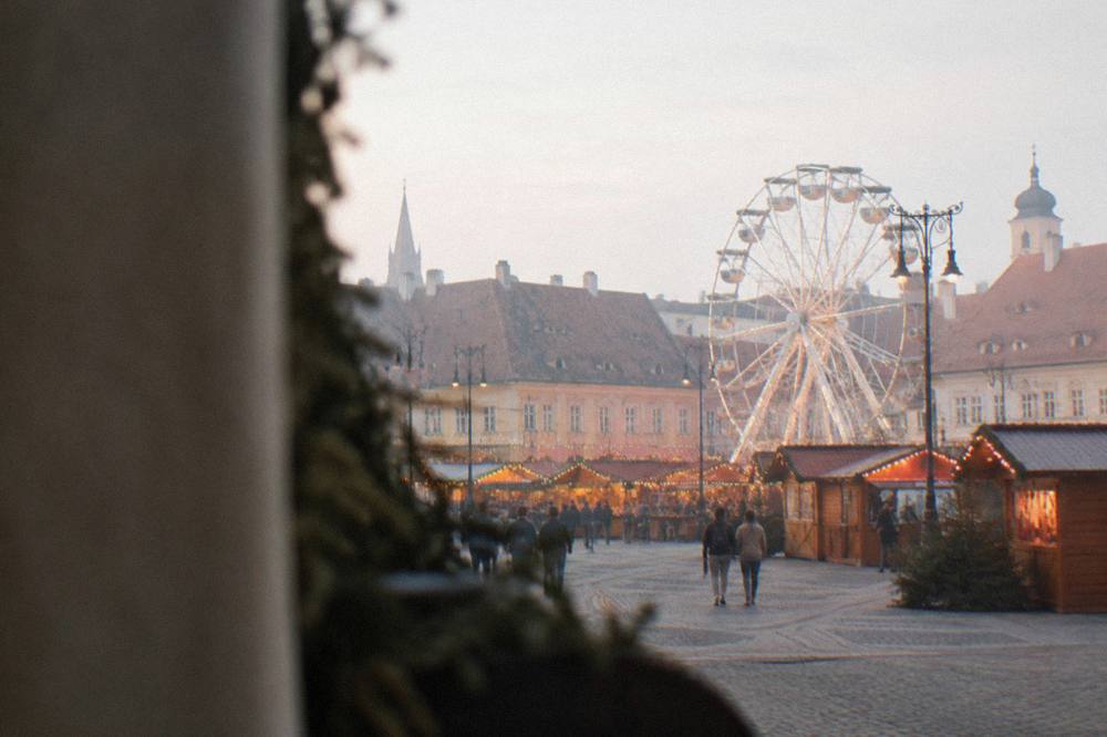Festive wooden stalls and a Ferris wheel in a lit-up grand square at dusk